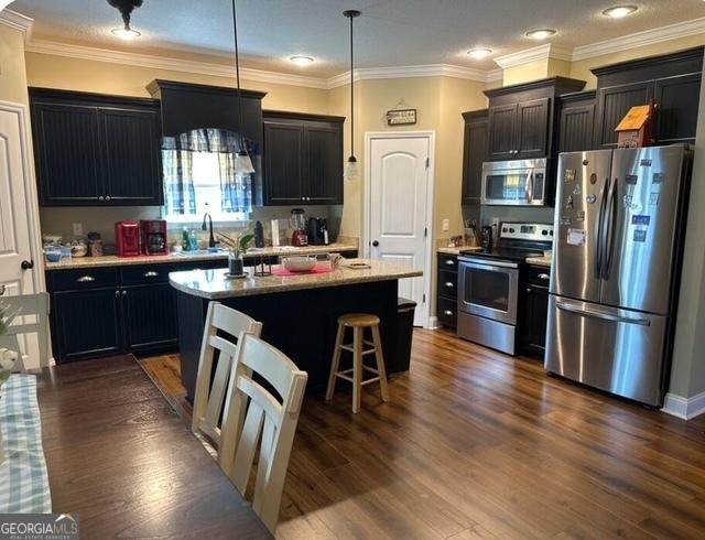 4961 Bentwood Ct, Valdosta, GA 31601 - kitchen with stainless steel appliances, a center island with sink, pendant lighting, a breakfast bar, and crown molding