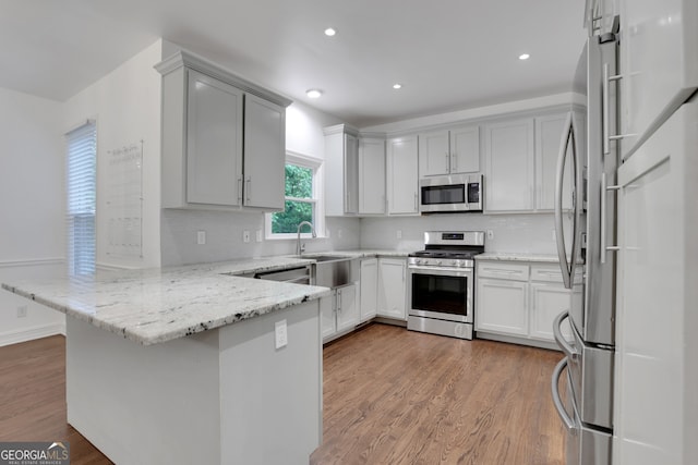 11280 Brookhollow Trl, Alpharetta, GA 30022 - kitchen with stainless steel appliances, a peninsula, tasteful backsplash, light stone countertops, and wood finished floors