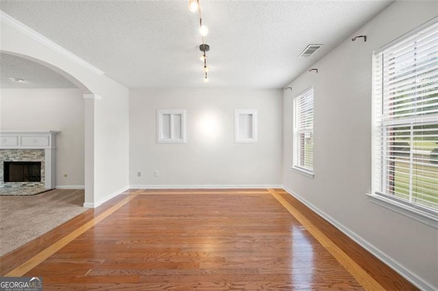 1486 Rogers Crossing Dr, Lithonia, GA 30058 - unfurnished living room featuring arched walkways, plenty of natural light, a textured ceiling, light wood-style flooring, and a fireplace