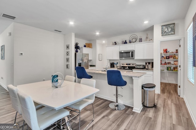 289 Pond Ct, Hoschton, GA 30548 - kitchen featuring appliances with stainless steel finishes, light wood-style flooring, an island with sink, white cabinetry, and a kitchen breakfast bar