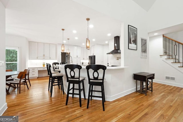 5535 Buck Hollow Dr, Alpharetta, GA 30005 - kitchen featuring wall chimney range hood, light wood-style floors, a peninsula, a kitchen bar, and recessed lighting