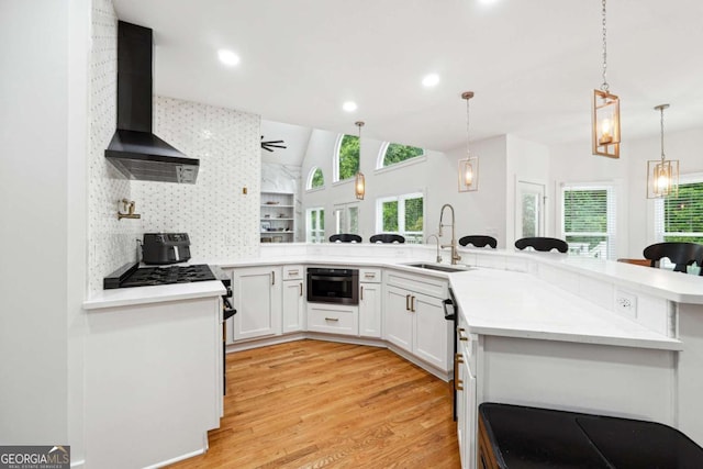 5535 Buck Hollow Dr, Alpharetta, GA 30005 - kitchen with wall chimney range hood, light wood-style flooring, vaulted ceiling, white cabinetry, and decorative light fixtures