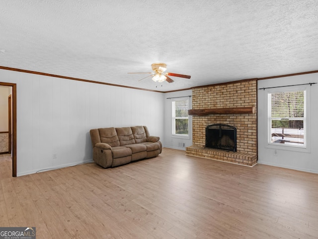 1001 Stagecoach Rd, Stockbridge, GA 30281 - unfurnished living room featuring light wood-style floors, a ceiling fan, a textured ceiling, a brick fireplace, and ornamental molding
