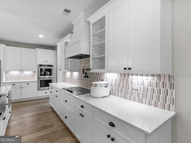 319 S Mount Carmel Rd, Mcdonough, GA 30253 - kitchen featuring stainless steel double oven, black electric stovetop, custom range hood, white cabinets, and tasteful backsplash