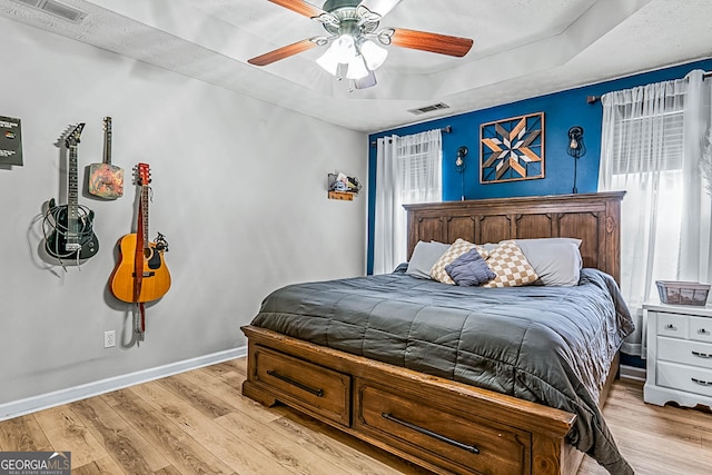 161 Mills Dr, Covington, GA 30016 - bedroom with light wood-style flooring, a tray ceiling, baseboards, and a ceiling fan