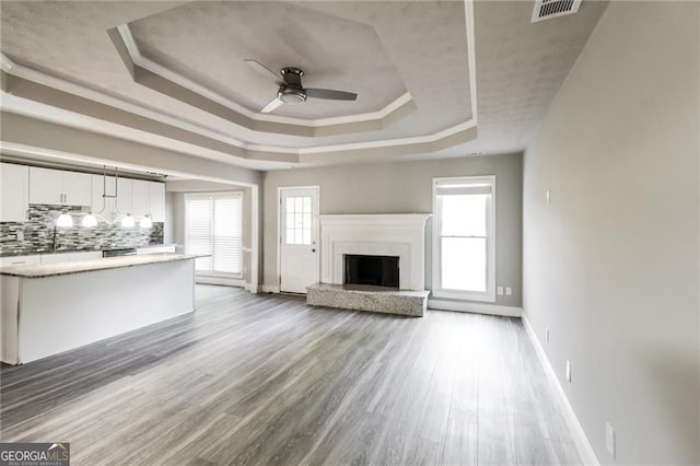 4820 Camden Dr SW, Conyers, GA 30094 - unfurnished living room with a tray ceiling, a ceiling fan, baseboards, wood finished floors, and a fireplace with raised hearth