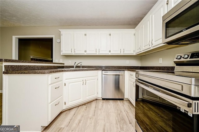 85 Chestnut Dr, Covington, GA 30016 - kitchen with appliances with stainless steel finishes, a sink, white cabinetry, light wood-style flooring, and dark countertops