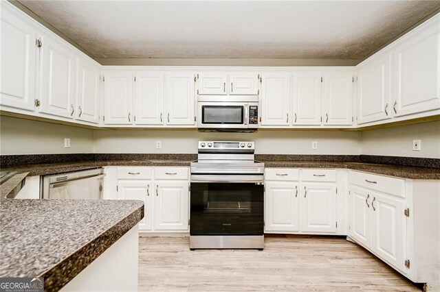 85 Chestnut Dr, Covington, GA 30016 - kitchen with stainless steel appliances, white cabinetry, light wood-style floors, and dark countertops