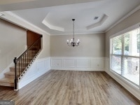 473 Cherry Creek Dr, Loganville, GA 30052 - unfurnished dining area with crown molding, wood finished floors, stairs, a chandelier, and a tray ceiling