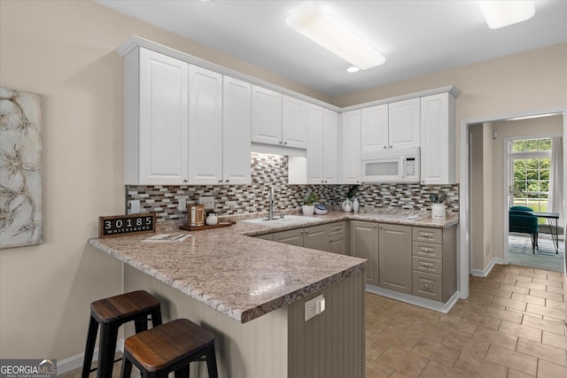 10 Wigwam Cir, Whitesburg, GA 30185 - kitchen with white microwave, decorative backsplash, a breakfast bar area, and white cabinets