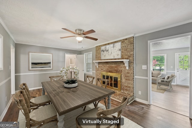 2676 Abington Dr, Snellville, GA 30078 - dining room featuring wood finished floors, a ceiling fan, a brick fireplace, crown molding, and baseboards