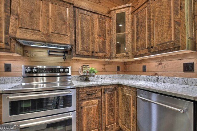 968 Hidden Valley Dr, Morganton, GA 30560 - kitchen featuring appliances with stainless steel finishes, exhaust hood, glass insert cabinets, light stone countertops, and wood walls