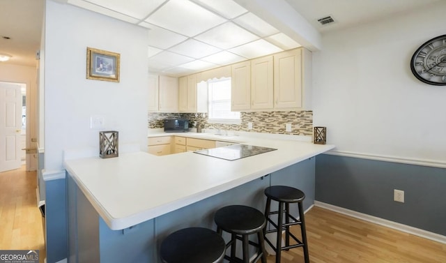 393 Arrowhead Trl, Eatonton, GA 31024 - kitchen with a kitchen bar, light wood-style floors, decorative backsplash, a peninsula, and black electric cooktop