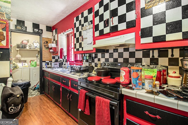 564 Peters St, Statham, GA 30666 - kitchen featuring washing machine and dryer, under cabinet range hood, tile countertops, stainless steel electric stove, and light wood-style flooring