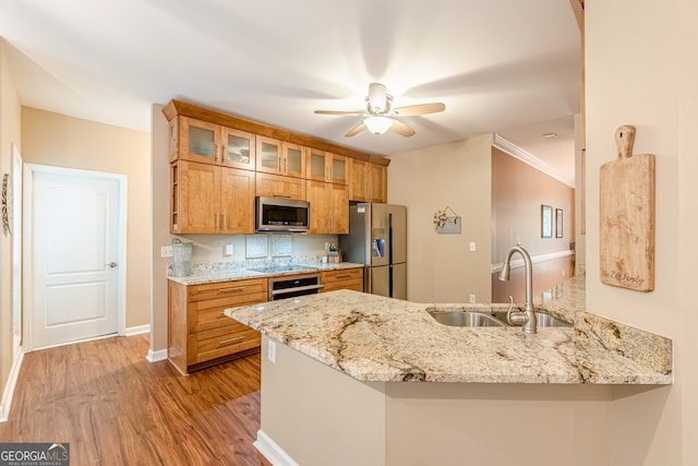 5767 Wembley Dr, Douglasville, GA 30135 - kitchen featuring appliances with stainless steel finishes, a peninsula, brown cabinetry, glass insert cabinets, and light wood-type flooring