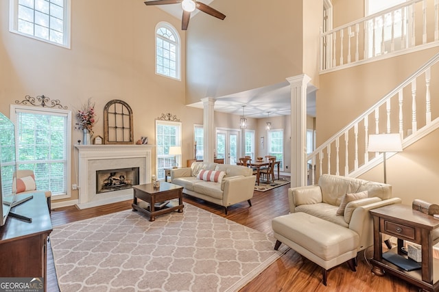 5767 Wembley Dr, Douglasville, GA 30135 - living room featuring a towering ceiling, ornate columns, a ceiling fan, wood finished floors, and a fireplace