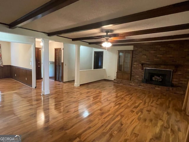 404 S Baker St, Glennville, GA 30427 - unfurnished living room with wood finished floors, beamed ceiling, ceiling fan, a brick fireplace, and a wainscoted wall
