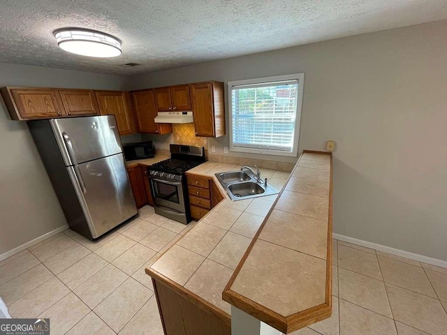 3251 Avensong Village Cir, Milton, GA 30004 - kitchen featuring appliances with stainless steel finishes, under cabinet range hood, tile counters, brown cabinetry, and light tile patterned flooring