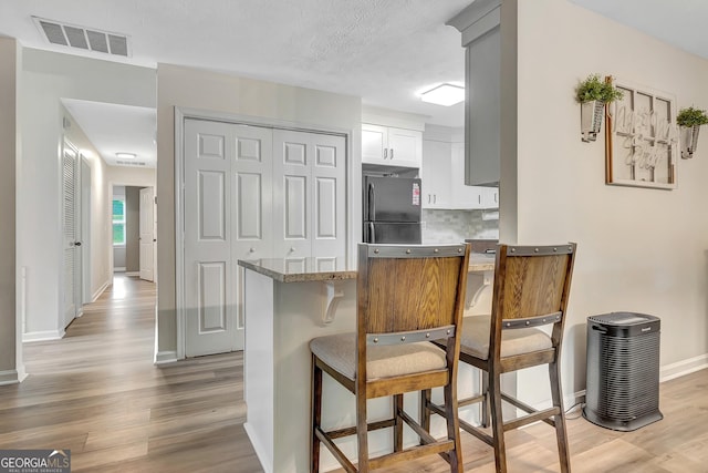 10 1st Ave E, Newnan, GA 30265 - kitchen with freestanding refrigerator, light wood-style floors, baseboards, tasteful backsplash, and a breakfast bar area