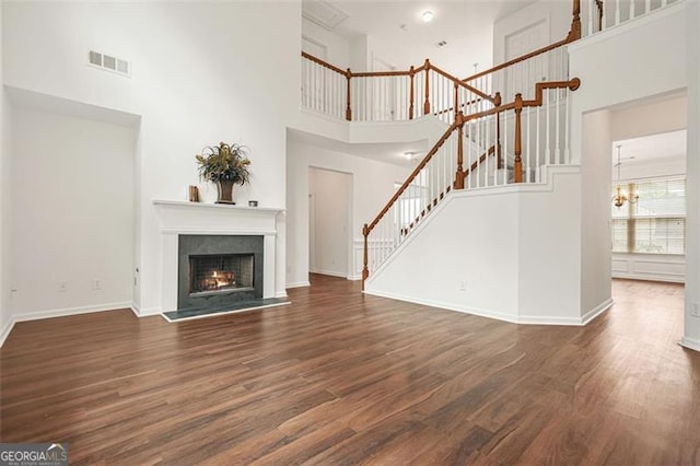 606 Hay Meadow Pl, Acworth, GA 30102 - unfurnished living room featuring a towering ceiling, stairs, wood finished floors, a warm lit fireplace, and baseboards