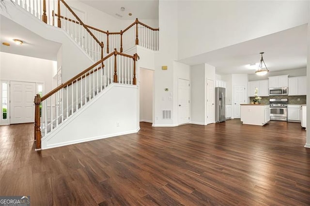 606 Hay Meadow Pl, Acworth, GA 30102 - unfurnished living room with a towering ceiling, stairs, dark wood-style floors, and baseboards