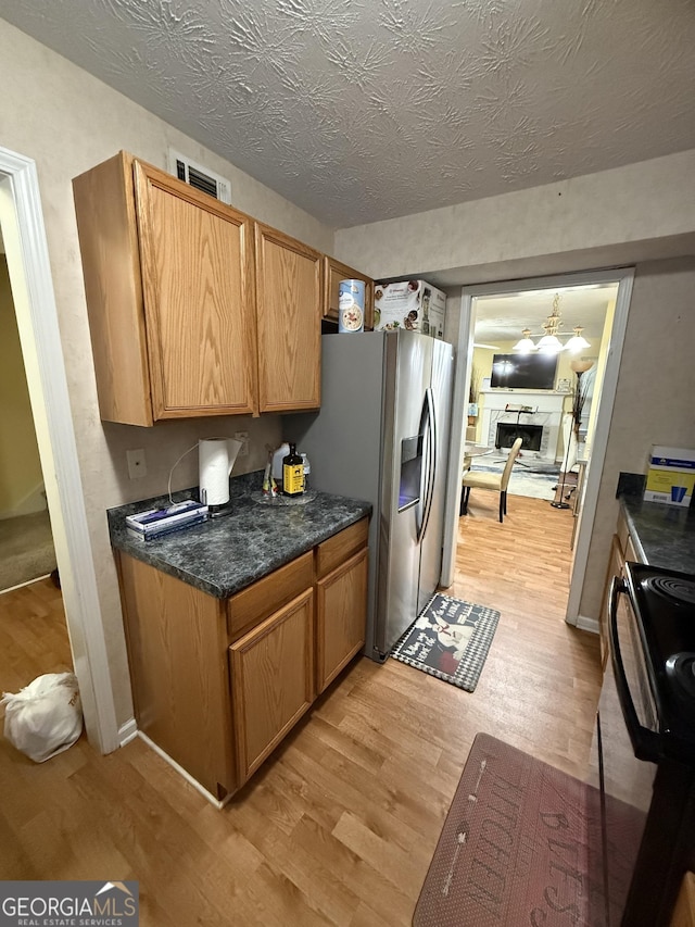 6550 Wellington Chase Ct, Lithonia, GA 30058 - kitchen with light wood-style floors, black range oven, stainless steel refrigerator with ice dispenser, a fireplace, and a textured ceiling