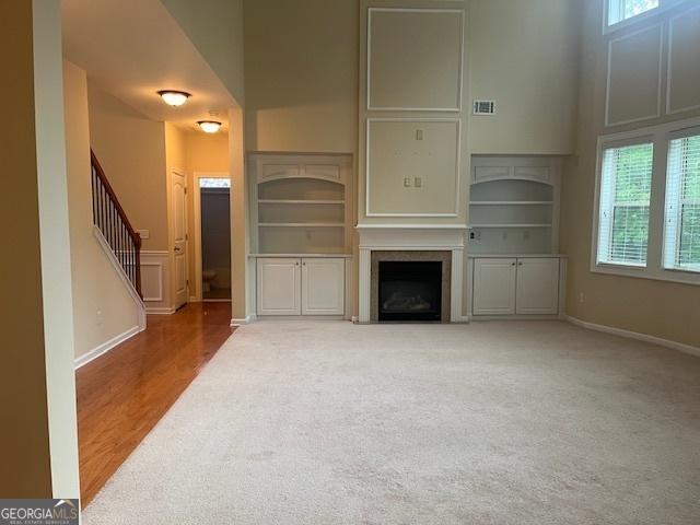 82 Sweetwater Way, Senoia, GA 30276 - unfurnished living room featuring a fireplace, built in shelves, a towering ceiling, carpet, and stairway