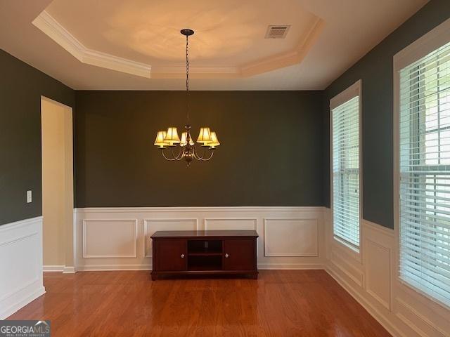 82 Sweetwater Way, Senoia, GA 30276 - unfurnished dining area featuring a tray ceiling, wood finished floors, a chandelier, a wainscoted wall, and a decorative wall
