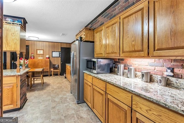 190 Roberts Way, Cornelia, GA 30531 - kitchen with stainless steel appliances, brown cabinetry, light stone counters, wood walls, and a textured ceiling