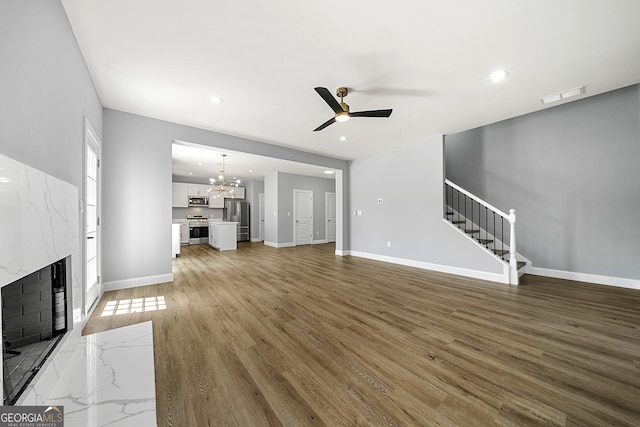 142 Arnco 3rd St, Newnan, GA 30263 - unfurnished living room featuring stairs, ceiling fan, a premium fireplace, a chandelier, and light wood-style floors