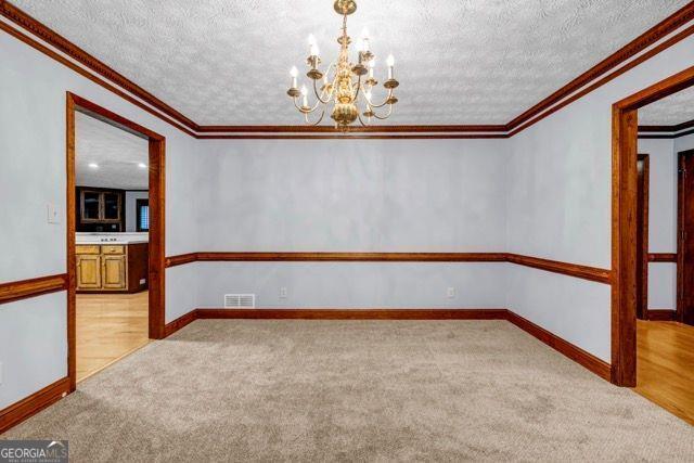 362 Clyde Ct, Mcdonough, GA 30252 - unfurnished room with ornamental molding, a chandelier, light carpet, a textured ceiling, and baseboards