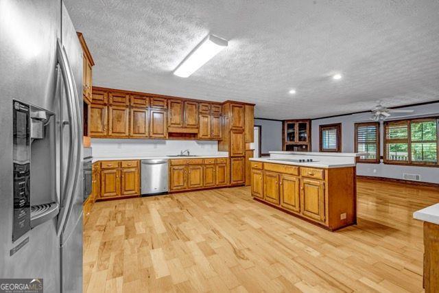 362 Clyde Ct, Mcdonough, GA 30252 - kitchen with stainless steel appliances, brown cabinets, light wood finished floors, a textured ceiling, and light countertops