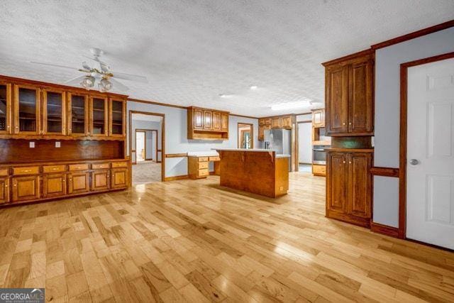 362 Clyde Ct, Mcdonough, GA 30252 - kitchen featuring light wood-style flooring, crown molding, brown cabinets, a center island, and a textured ceiling