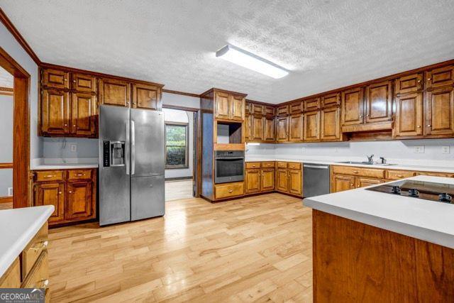 362 Clyde Ct, Mcdonough, GA 30252 - kitchen with stainless steel appliances, light wood finished floors, a textured ceiling, brown cabinetry, and light countertops