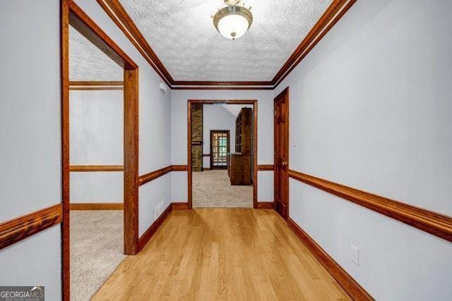 362 Clyde Ct, Mcdonough, GA 30252 - hallway featuring a textured ceiling, ornamental molding, light wood-style floors, baseboards, and light carpet