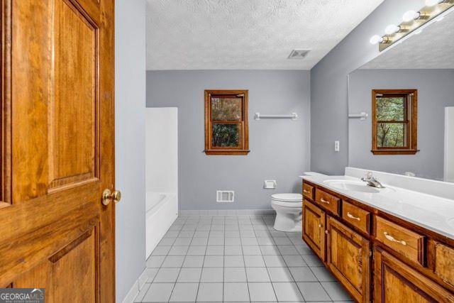 362 Clyde Ct, Mcdonough, GA 30252 - bathroom with toilet, vanity, a textured ceiling, a bath, and baseboards