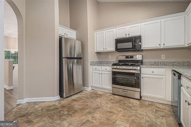 1501 Buckingham Pl, Stockbridge, GA 30281 - kitchen with appliances with stainless steel finishes, arched walkways, white cabinetry, light stone finish flooring, and lofted ceiling
