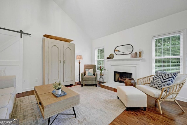 5421 Amherst Way, Flowery Branch, GA 30542 - living area featuring a fireplace with flush hearth, high vaulted ceiling, wood finished floors, a barn door, and baseboards