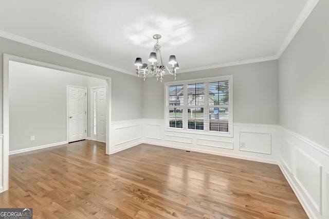 327 Oakland Bay Ct, Loganville, GA 30052 - unfurnished dining area with a chandelier, crown molding, wainscoting, wood finished floors, and a decorative wall