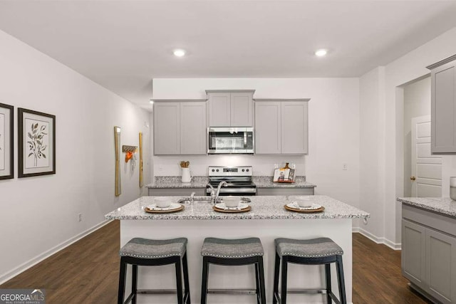 1311 Aura Ln, Lawrenceville, GA 30045 - kitchen featuring appliances with stainless steel finishes, gray cabinetry, a kitchen bar, light stone counters, and a center island with sink
