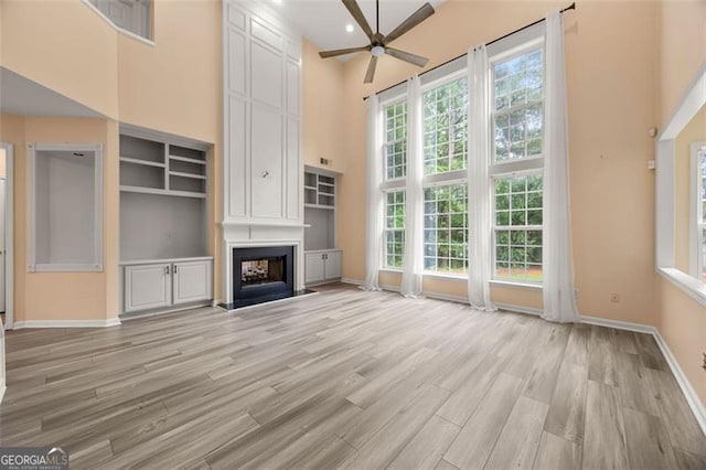 5156 Amberden Hall Dr, Suwanee, GA 30024 - unfurnished living room with a ceiling fan, a high ceiling, light wood-style flooring, a large fireplace, and built in features