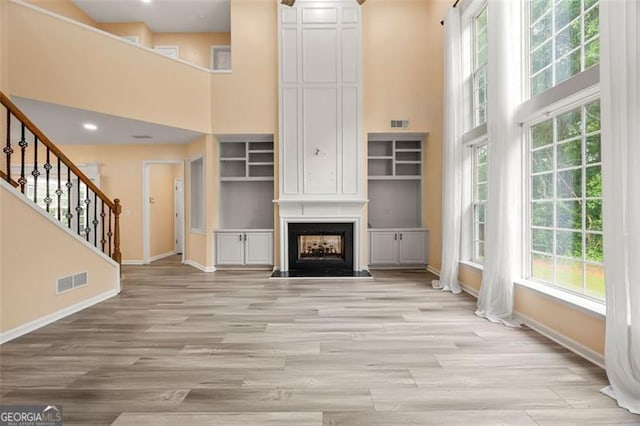 5156 Amberden Hall Dr, Suwanee, GA 30024 - unfurnished living room with a towering ceiling, healthy amount of natural light, light wood-style floors, stairs, and a fireplace
