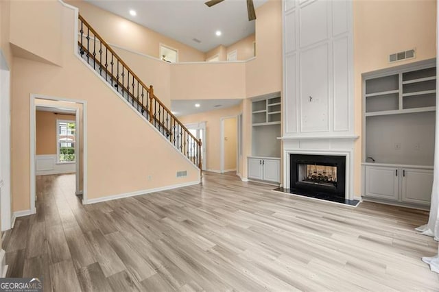 5156 Amberden Hall Dr, Suwanee, GA 30024 - unfurnished living room with light wood finished floors, stairway, a towering ceiling, a multi sided fireplace, and ceiling fan