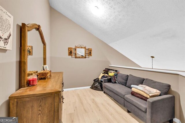 6504 Samoa, Flowery Branch, GA 30542 - living room featuring light wood finished floors, lofted ceiling, a textured ceiling, and baseboards