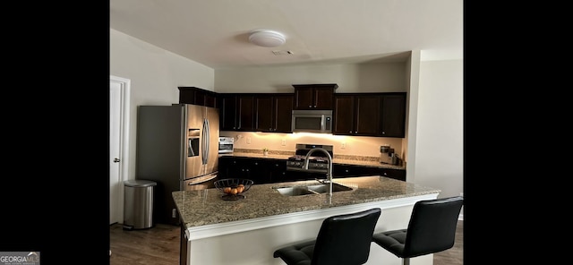 4241 Swamp Cypress Trl, Gainesville, GA 30504 - kitchen featuring stainless steel appliances, a kitchen bar, wood finished floors, light stone countertops, and an island with sink