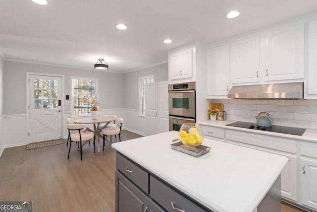 935 Old Loganville Rd, Loganville, GA 30052 - kitchen featuring stainless steel double oven, black electric cooktop, under cabinet range hood, crown molding, and white cabinetry