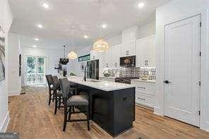 1464 Ezra Church Dr NW, Atlanta, GA 30314 - kitchen with a center island with sink, light wood-type flooring, a kitchen breakfast bar, white cabinets, and pendant lighting