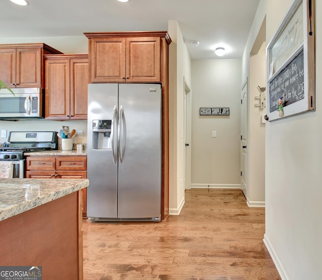 149 Horizon Hl, Newnan, GA 30265 - kitchen featuring stainless steel appliances, brown cabinetry, light wood-style flooring, light stone countertops, and baseboards