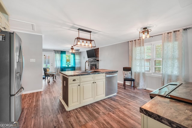 113 Fletcher Rd, Eatonton, GA 31024 - kitchen featuring stainless steel appliances, a brick fireplace, wood finished floors, cream cabinets, and a center island with sink