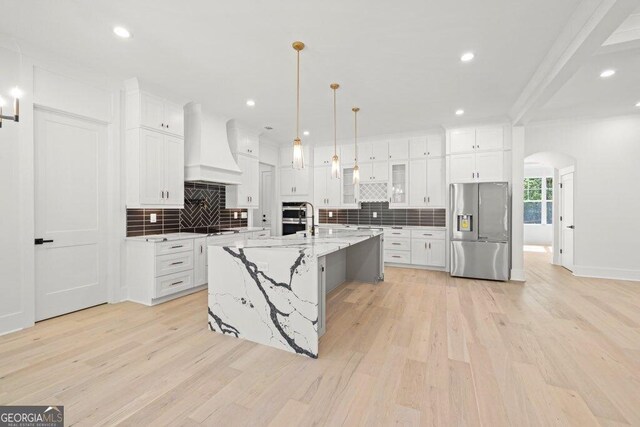 1387 Mineral Springs Rd, Hoschton, GA 30548 - kitchen with stainless steel appliances, premium range hood, arched walkways, light wood finished floors, and decorative backsplash